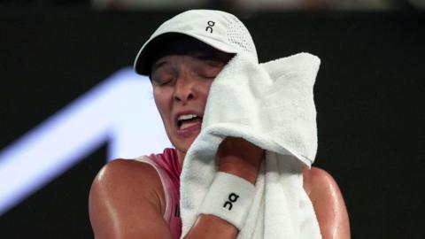 Iga Swiatek rubs her face with a towel at the 2025 Australian Open