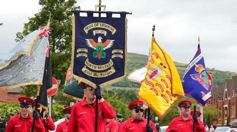 A group of men in red shirts and red hats holding banner during a parade in north Belfast