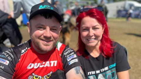 Gerrard Fox and Martina Kavanagh smile, they wear colourful bike t-shirts. He wears a cap, she has bright red hair and wears sunglasses.

