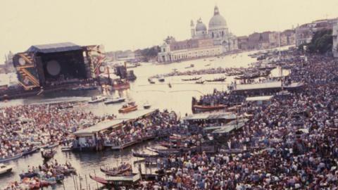 Crowds of people, the Venice skyline in the background and a large open-air stage