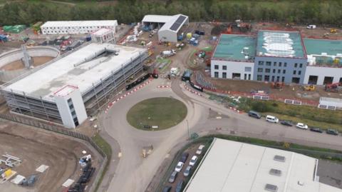 A construction site with a roundabout in the middle and buildings surrounding it.