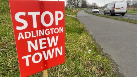 A sign next to a busy road which says stop Adlington new town