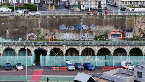 A high up shot of the terrace with two workers standing on it. The bottom of the terrace has fences covering it up