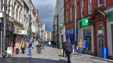 High street in Douglas. People are walking through the shopping street with shopping bags.
