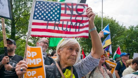 A woman holds an American flag saying 'No To Trump' at a protest in Edinburgh
