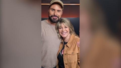 A man with brown facial hair embraces a woman with dirty blonde hair