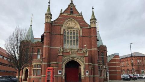 The Town Hall Theatre is redbrick and has an arch and an ornate arched window. There is an old-style red phone box outside