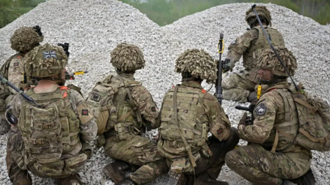 Soldiers in camouflage crouching by gravel 