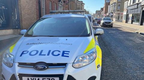 Police car in a street with shops and flats.