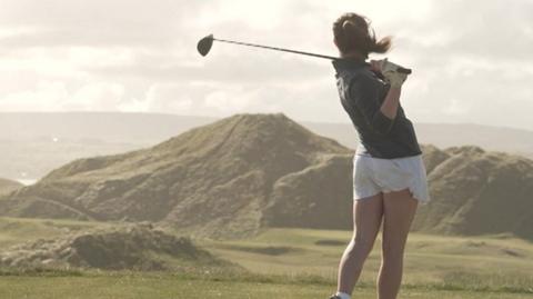 A girl tees off at golf