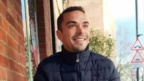 A smiling Leonard Farruku looks off to the side of the camera. He has smartly cropped dark hair and a stubble goatee beard. He is wearing a navy blue padded winter jacket, zipped up to his chin.