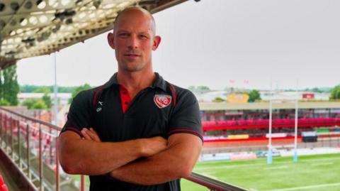 Wayne Thompson standing in the stand at Kingsholm with his arms folded