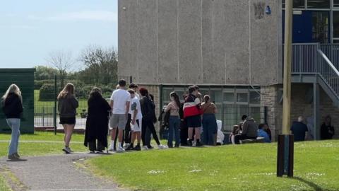 Queue of students heading in to get the antibiotics at a school in Weymouth. It is a sunny day.