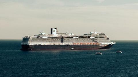 A large cruise ship on a sunny day with two tender vessels headed towards it.