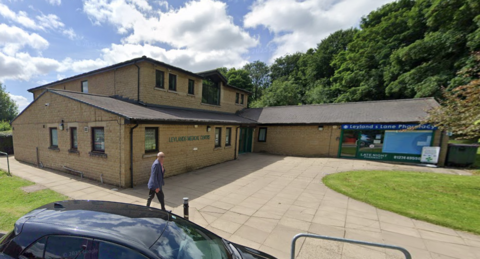 Image of two storey stone built medical centre adjoined by small pharmacy building set in lawned gardens.