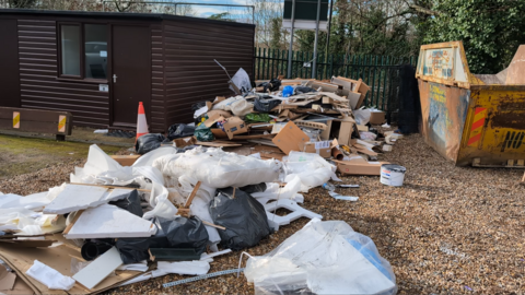 A huge pile of rubbish, including black bags and bits of wood, discarded on the ground.