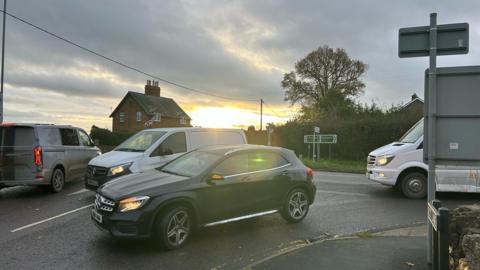 Cars at a busy road junction with the sun rising in the background and a white minibus on the road behind
