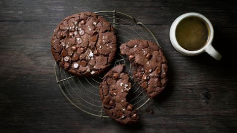 chocolate chip cookies on a cooling rack next to a mug of coffee on a dark wooden background.