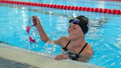 Swimmer Suzanna Hext in the pool wearing a swimming hat and holding something that it is not clear to see