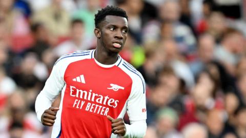 Eddie Nketiah, wearing Arsenal's red and white home kit, has his arms partly outstretched as if he was slowing down from a run