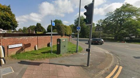 Road junction with traffic lights and pavement curving around a traffic light crossing point.