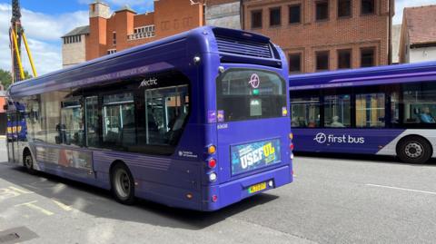 This image shows purple-painted buses heading in both directions along York's Rougier Street, where there are plans to restrict access to some vehicles to speed up bus journey times. A crane can be seen to the left of the picture.