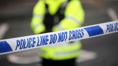 Generic shot of a police cordon with an officer standing in high-vis in the background, out of focus