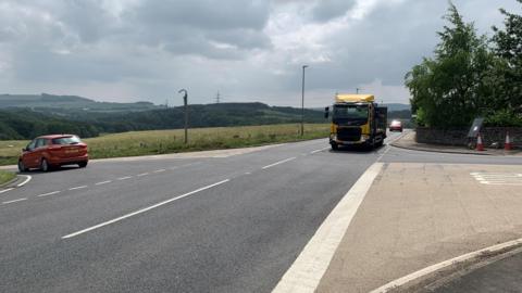 Hazlehead Crossroads on the A616. It is a rural area. A red car turns left as a yellow HGV approaches the junction.