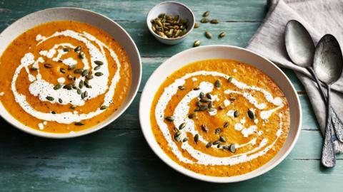 Two bowls of pumpkin soup with cream drizzled on top.