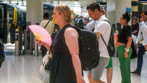 A commuter cools with a hand fan at Waterloo station struggle in in the sweltering heat as the hot weather continues. The Met Office issues a red extreme heat warning for London and South of England with temperatures et to reach 36 Celsius today. Date created: Jun 26 2026