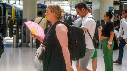 A commuter cools with a hand fan at Waterloo station struggle in in the sweltering heat as the hot weather continues. The Met Office issues a red extreme heat warning for London and South of England with temperatures et to reach 36 Celsius today. Date created: Jun 26 2026