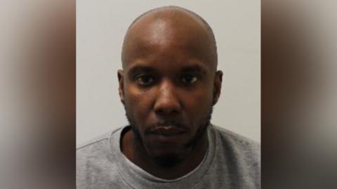 A mugshot of Owusu in a grey crewneck shirt. He stares blankly at the camera.