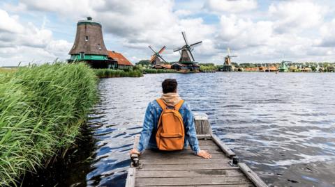 Man sitting on wooden jetty looking across to three windmills 