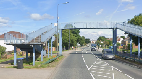 The Quarry House Lane Footbridge is a blue metal structure over a road, with a staircase on either side.
