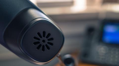 A close up image of the mouthpiece on black landline phone. The blurred background shows the console. 