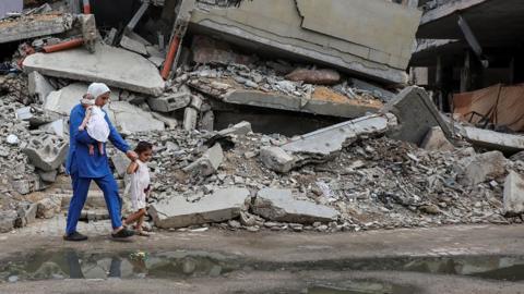 A displaced Palestinian mother and children walk past the rubble of a house destroyed in an Israeli strike on 1 September 2024