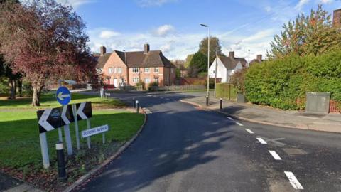 Roundabout with road sign and house in the sunshine in the distance