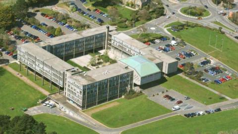 An aerial view of Cornwall Council offices, a three to five storey courtyard surrounded by 60s concrete buildings, set among a grass area and carpark.