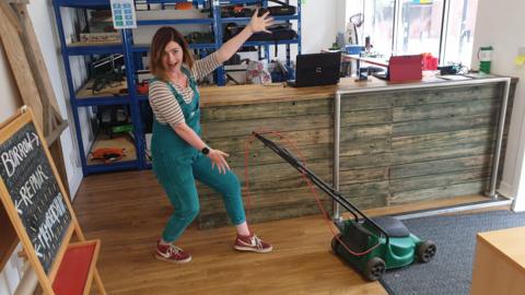 A woman striking a joyful pose standing next to a lawnmower