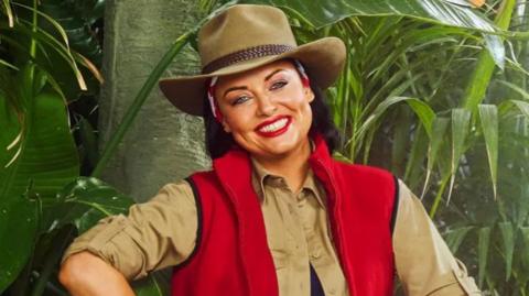A photograph of Shona on I'm a Celebrity. She is smiling and wearing red lipstick.
