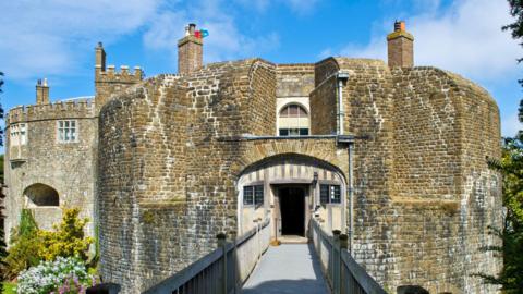 The entrance to a round, brick, Tudor castle. The bricks are yellow in colour and the building is pictured on a clear day.
