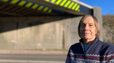 The picture shows Brian Maddison, who is a former British Rail engineer. In the background is the bridge, which also allows road vehicles to travel underneath, along the A5. This is the bridge at Hinckley in Leicestershire. 