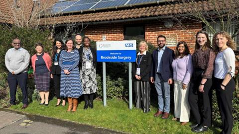 The staff at Brookside surgery in Earley, Berkshire standing outside the practice and smiling at the camera next to the NHS sign.