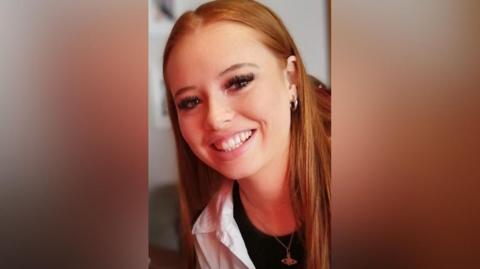 A young woman with long red hair smiles at the camera