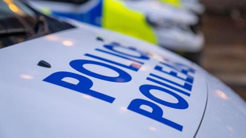 Police vehicles with the word 'police' in bold blue letters on the white bonnet in the foreground.