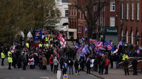 A large group of people carrying a mix of flags, including the Cross of St George and the Union flag, are outside Nuneaton Town Hall