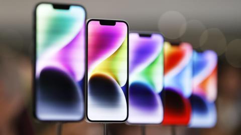 Five Iphones on display in a shop. They have multicoloured waves on their screens and are place upon pedestals