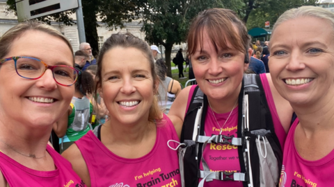 Ms Wrathall smiles into the camera with a friend standing to her left and two women standing to her right. They're all wearing pint Brain Tumour Research running vests.