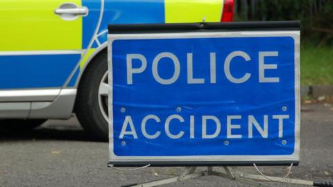 Police accident sign - blue with a silver trim and silver words - next to a blue and yellow police car