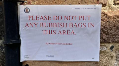 A laminated sign on a wall which reads 'Please do not put any rubbish bags in this area'